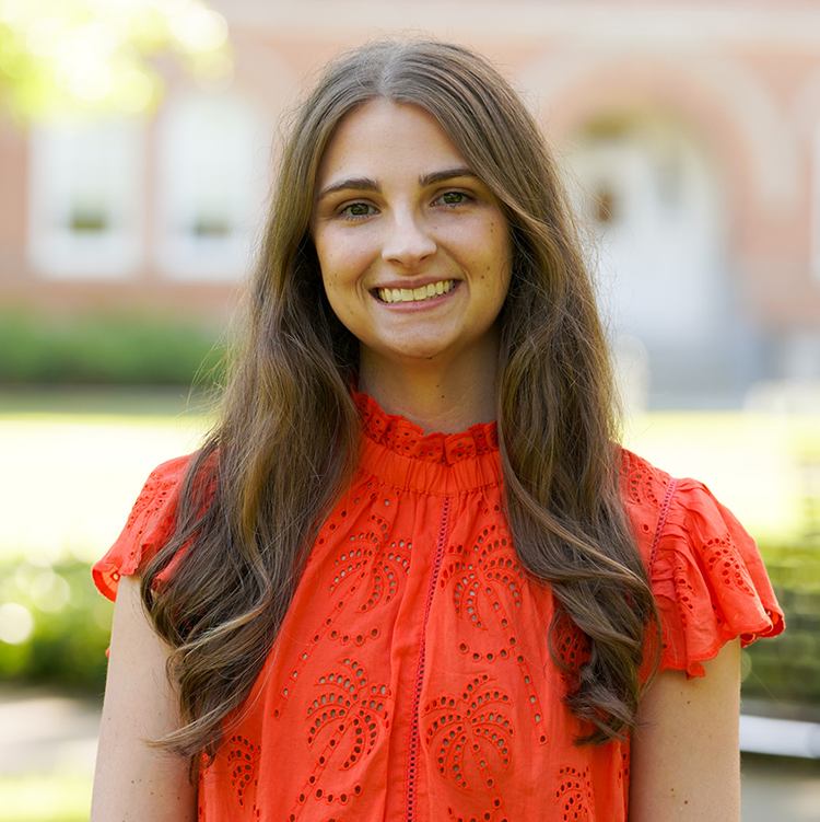 Photograph: Smiling young woman with long brown hair in a ruffled red top, outdoors.