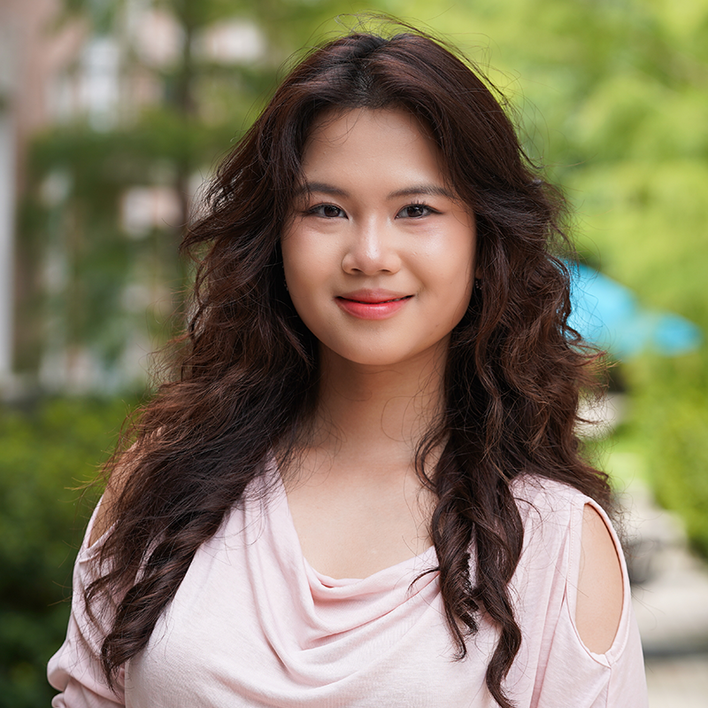 Young person smiling, wearing a light pink/off white shirt in an outdoor setting