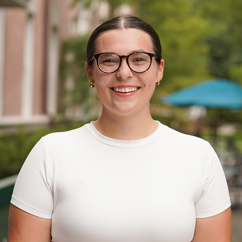 Young person smiling, wearing a white shirt in an outdoor setting